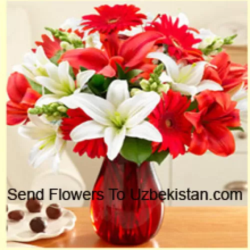 Gerberas rouges, lys blancs, lys rouges et autres fleurs assorties disposées magnifiquement dans un vase en verre